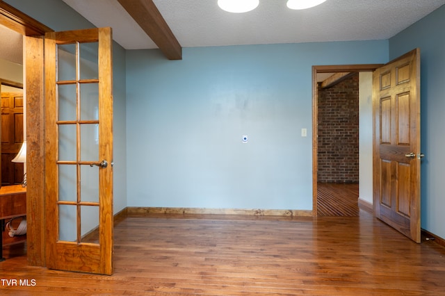 spare room featuring hardwood / wood-style flooring, beam ceiling, and a textured ceiling