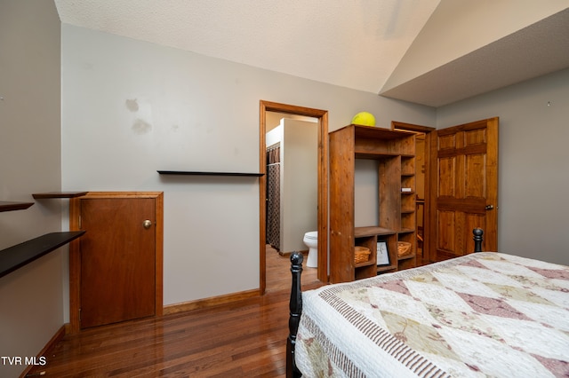 bedroom featuring a textured ceiling, dark hardwood / wood-style flooring, ensuite bath, and vaulted ceiling