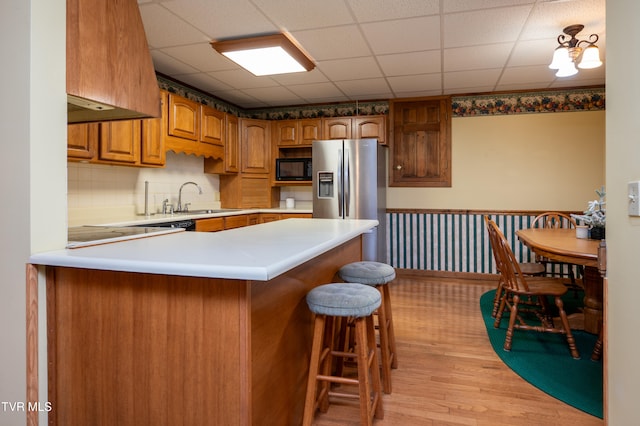 kitchen with sink, a breakfast bar area, light hardwood / wood-style flooring, kitchen peninsula, and black microwave