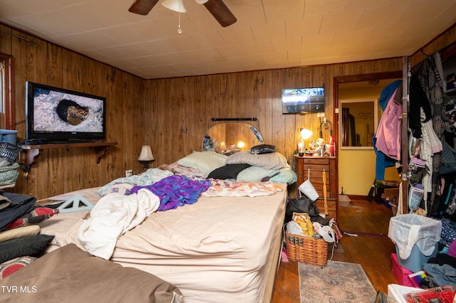 bedroom featuring ceiling fan, dark hardwood / wood-style flooring, and wooden walls