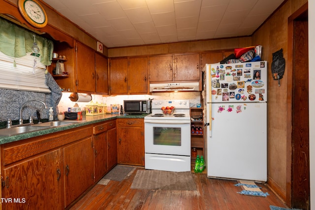 kitchen featuring tasteful backsplash, white appliances, dark wood-type flooring, sink, and wood walls