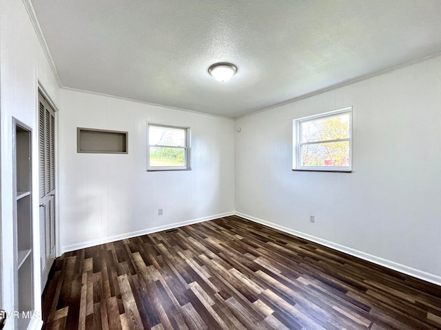 spare room featuring a textured ceiling, dark hardwood / wood-style flooring, crown molding, and a healthy amount of sunlight