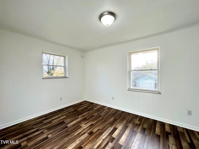 spare room featuring a healthy amount of sunlight, crown molding, and dark wood-type flooring