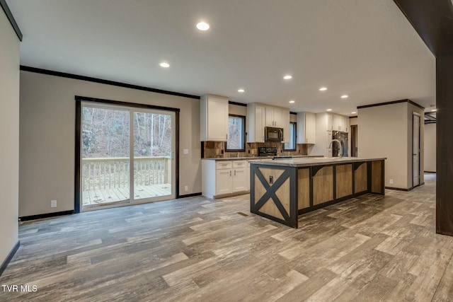 kitchen with tasteful backsplash, an island with sink, white cabinets, ornamental molding, and electric range