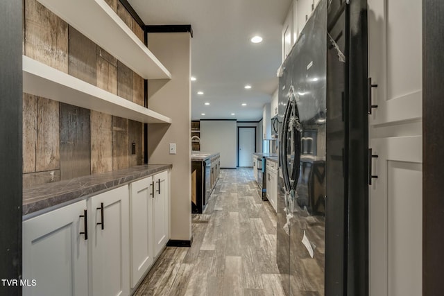 interior space featuring sink, white cabinetry, light hardwood / wood-style floors, black refrigerator with ice dispenser, and dark stone counters