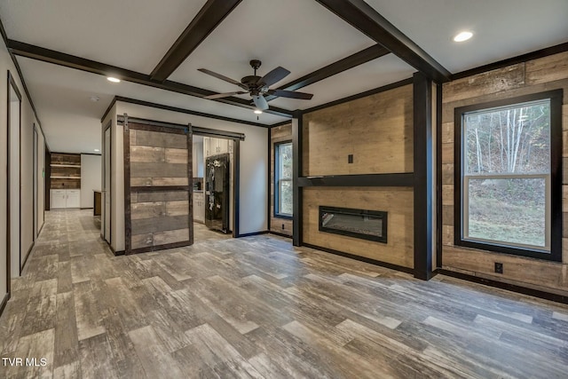 unfurnished living room with ceiling fan, a barn door, hardwood / wood-style floors, and beam ceiling