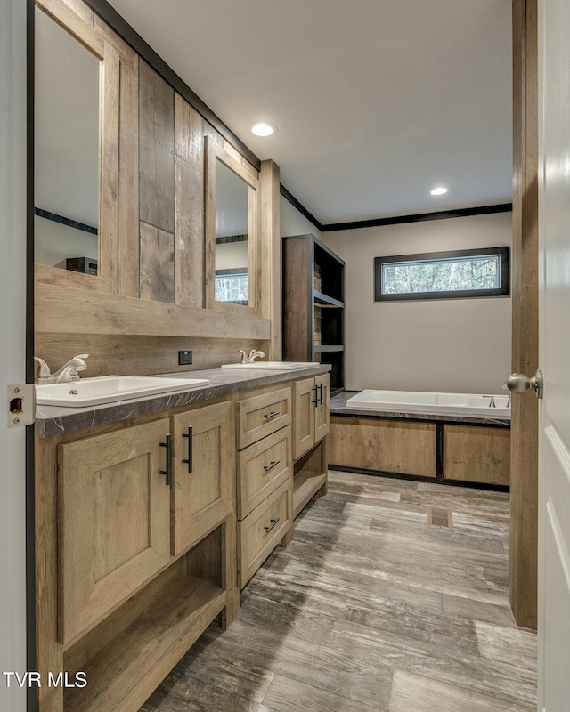 bathroom with crown molding, vanity, a bathing tub, and wood-type flooring