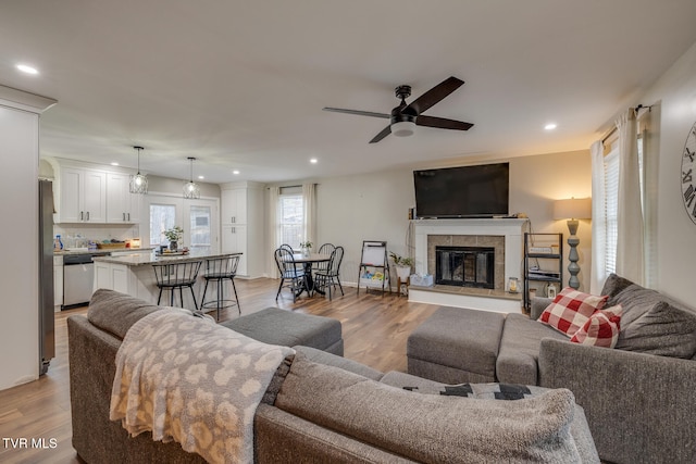 living room featuring light hardwood / wood-style floors, ceiling fan, and a tiled fireplace