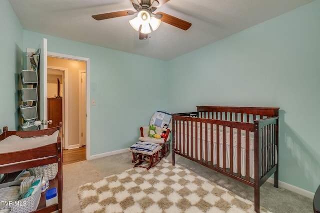 bedroom with ceiling fan, a crib, and light carpet