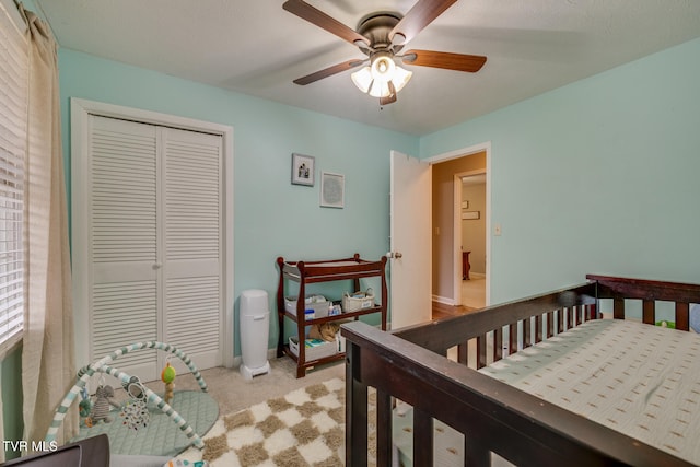 carpeted bedroom featuring ceiling fan, a closet, and a crib