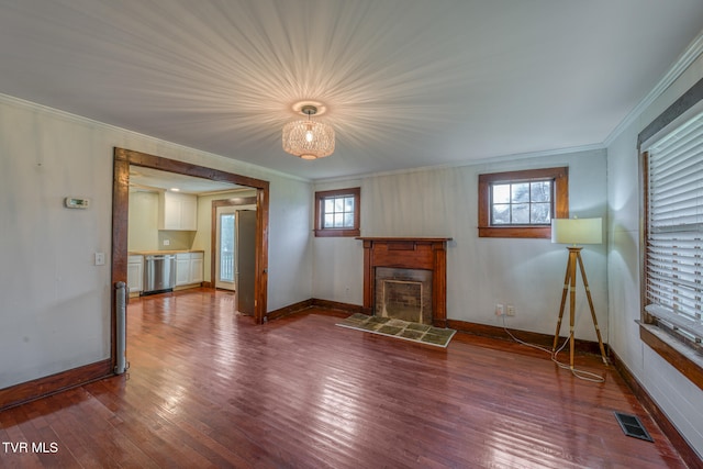 unfurnished living room featuring hardwood / wood-style floors, plenty of natural light, ornamental molding, and a tiled fireplace