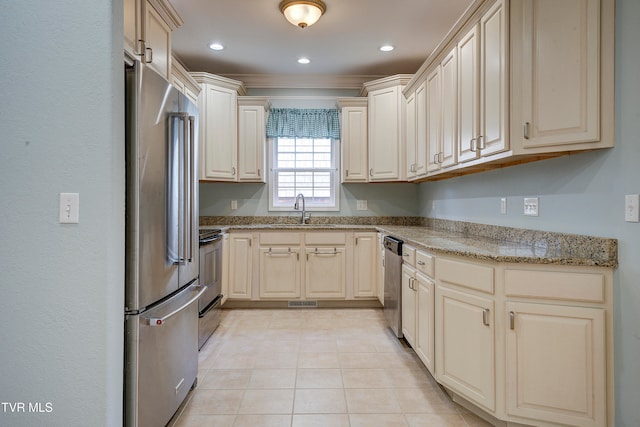 kitchen with light stone countertops, stainless steel appliances, sink, light tile patterned floors, and cream cabinets