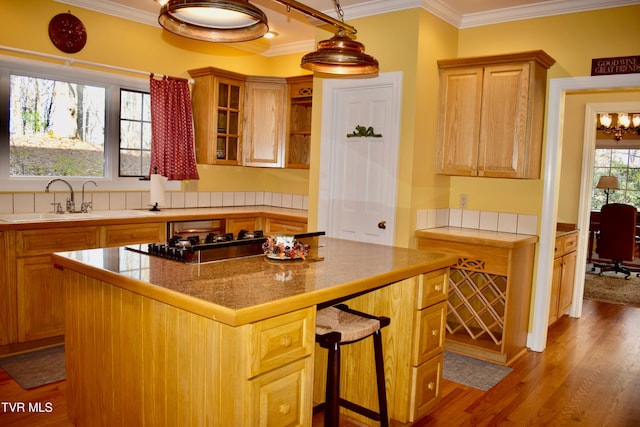 kitchen featuring crown molding, sink, hardwood / wood-style flooring, a kitchen island, and a breakfast bar area