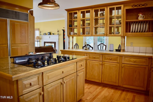 kitchen featuring black gas cooktop, a brick fireplace, paneled refrigerator, light wood-type flooring, and ornamental molding