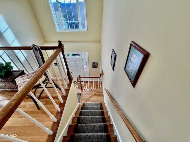 staircase featuring a towering ceiling, a healthy amount of sunlight, and wood-type flooring