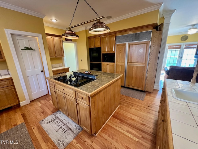 kitchen with pendant lighting, a center island, black appliances, ornamental molding, and light hardwood / wood-style floors