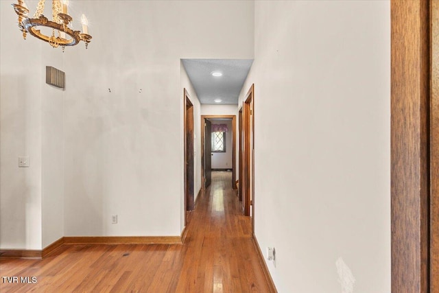 corridor with hardwood / wood-style flooring and a notable chandelier