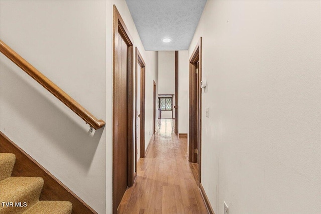 corridor with a textured ceiling and light wood-type flooring