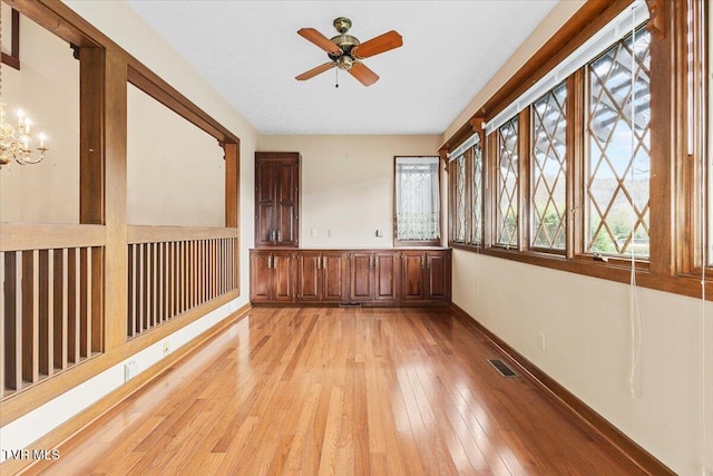 empty room featuring ceiling fan with notable chandelier and light wood-type flooring