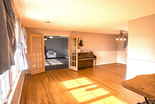 unfurnished living room featuring hardwood / wood-style flooring, ceiling fan with notable chandelier, and french doors