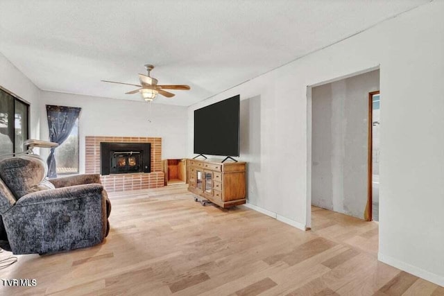 living room with ceiling fan, light hardwood / wood-style floors, a textured ceiling, and a brick fireplace