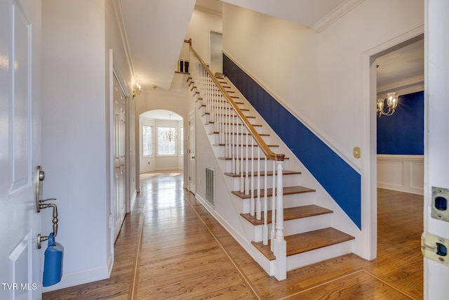 stairway with an inviting chandelier, ornamental molding, and hardwood / wood-style flooring