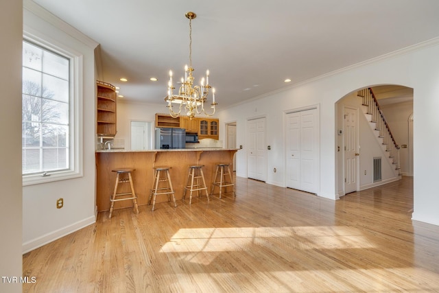 kitchen with kitchen peninsula, ornamental molding, light hardwood / wood-style floors, stainless steel refrigerator, and a breakfast bar area