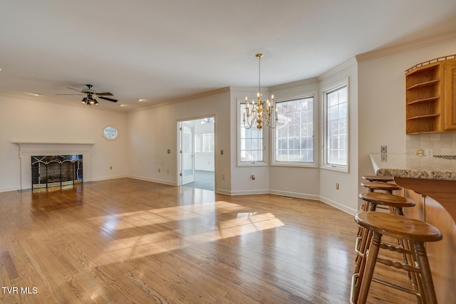 dining space with a premium fireplace, crown molding, light hardwood / wood-style floors, and ceiling fan with notable chandelier