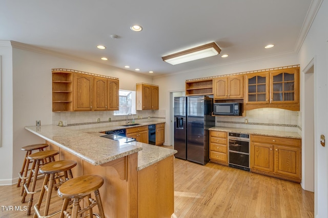 kitchen with black appliances, a kitchen breakfast bar, crown molding, sink, and light hardwood / wood-style flooring