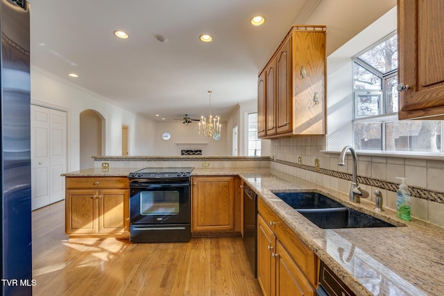 kitchen with tasteful backsplash, sink, black appliances, pendant lighting, and light hardwood / wood-style flooring