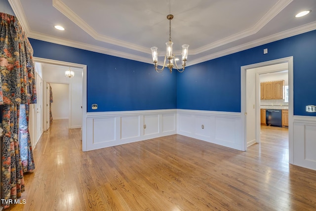 empty room featuring ornamental molding, a tray ceiling, light hardwood / wood-style flooring, and a notable chandelier