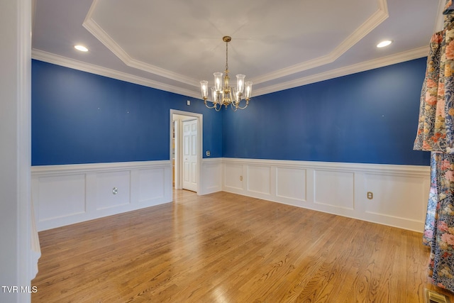 unfurnished room with a chandelier, a tray ceiling, light hardwood / wood-style flooring, and ornamental molding