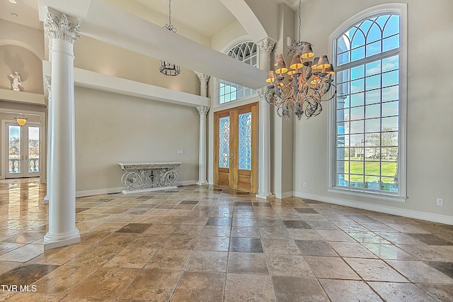 entryway featuring decorative columns, french doors, a high ceiling, and a chandelier