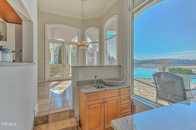 kitchen with a water view, sink, decorative light fixtures, ornamental molding, and a notable chandelier