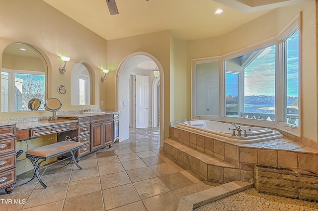 bathroom featuring tiled bath, vanity, a water view, and ceiling fan