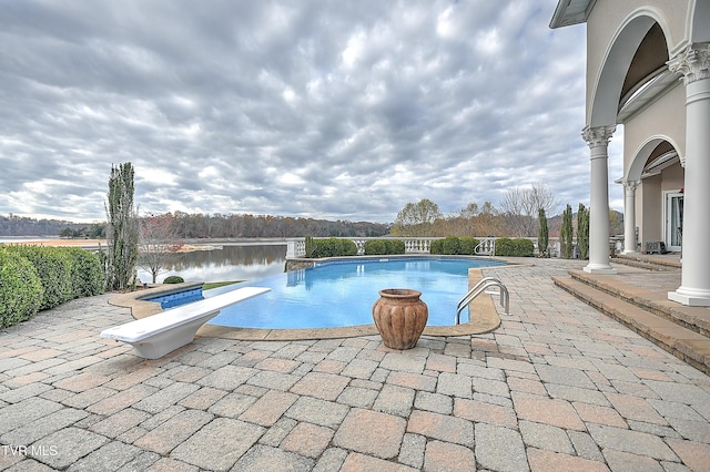 view of pool with a diving board, a water view, and a patio area