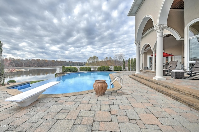 view of pool featuring a water view, a diving board, and a patio area