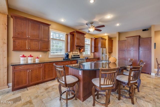 kitchen with sink, a breakfast bar area, stainless steel gas range oven, an island with sink, and dark stone counters