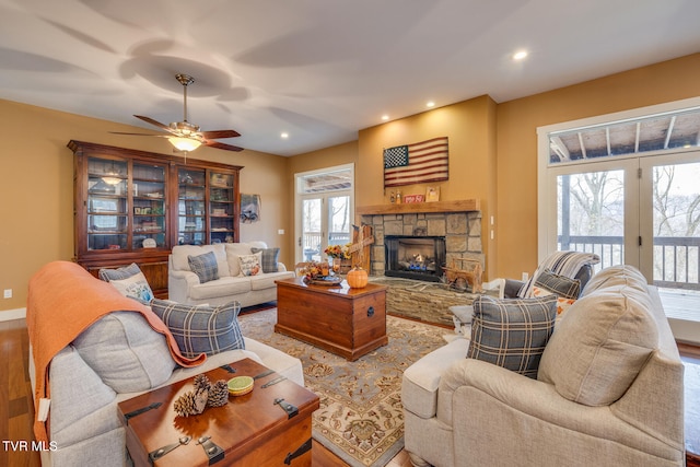 living room featuring wood-type flooring, a stone fireplace, and ceiling fan