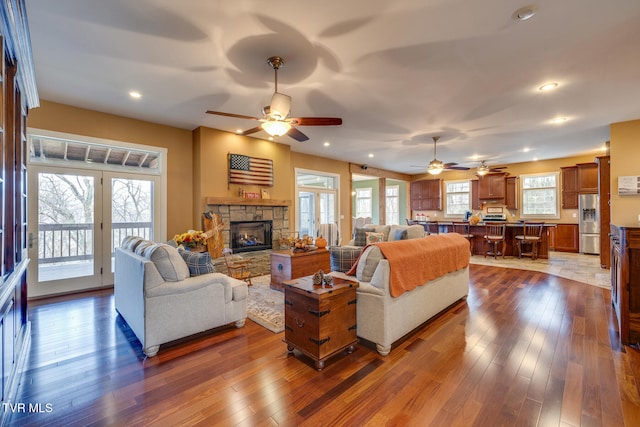 living room featuring ceiling fan, wood-type flooring, and a stone fireplace