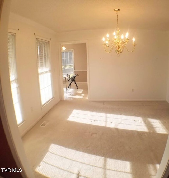 carpeted spare room featuring an inviting chandelier