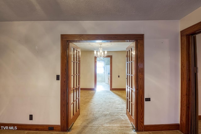 corridor with a chandelier, french doors, light colored carpet, and a textured ceiling