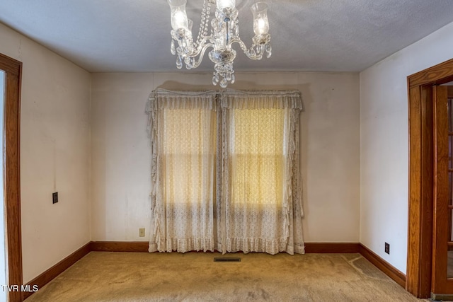 spare room with carpet, a textured ceiling, and a notable chandelier