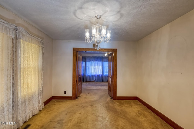 unfurnished dining area featuring a textured ceiling, light colored carpet, and an inviting chandelier