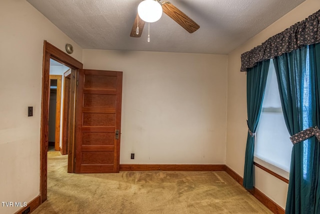 empty room with ceiling fan, light colored carpet, and a textured ceiling