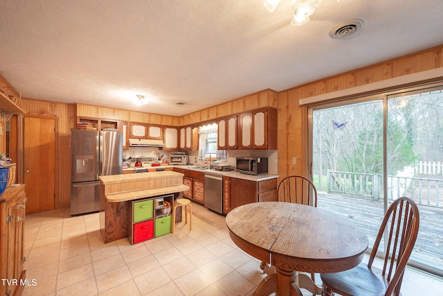 kitchen with wooden walls, a kitchen island, a textured ceiling, and appliances with stainless steel finishes