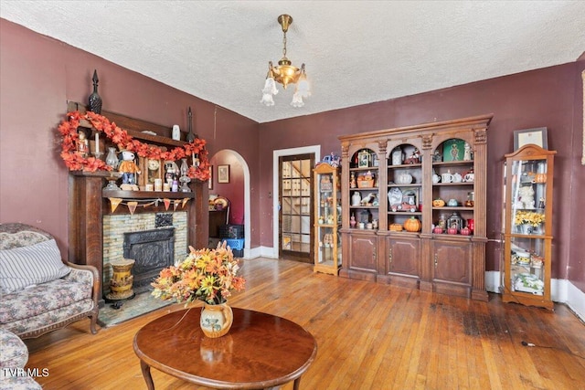 living room with a notable chandelier, wood-type flooring, a textured ceiling, and a brick fireplace