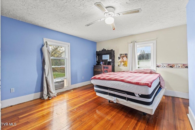 bedroom with multiple windows, ceiling fan, a textured ceiling, and hardwood / wood-style flooring