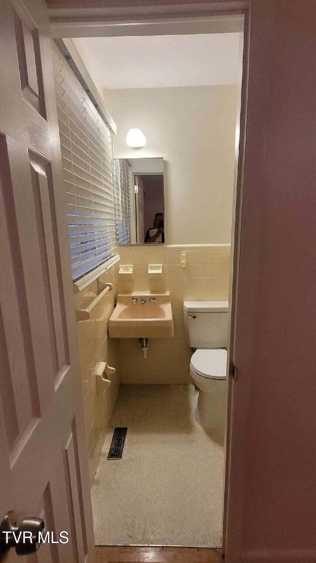 bathroom with toilet, sink, and tile walls