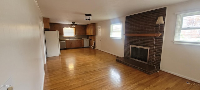 unfurnished living room with ceiling fan, a healthy amount of sunlight, light wood-type flooring, and a brick fireplace